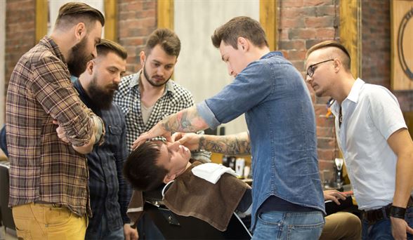 barber shaving a man's face while students watch