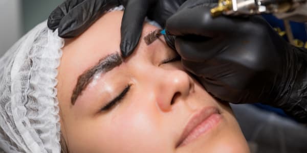 makeup artist applying permanent makeup to a woman's eyebrows