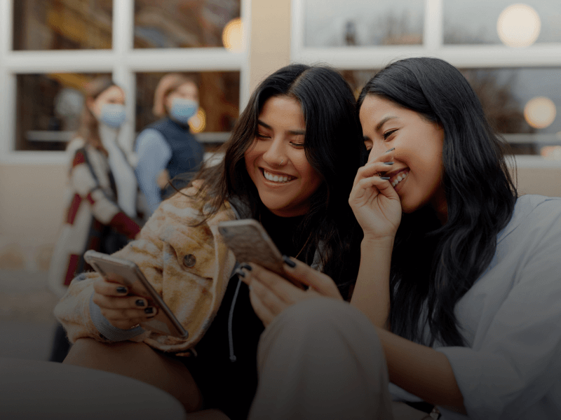 a couple of students sitting outside looking at their phones